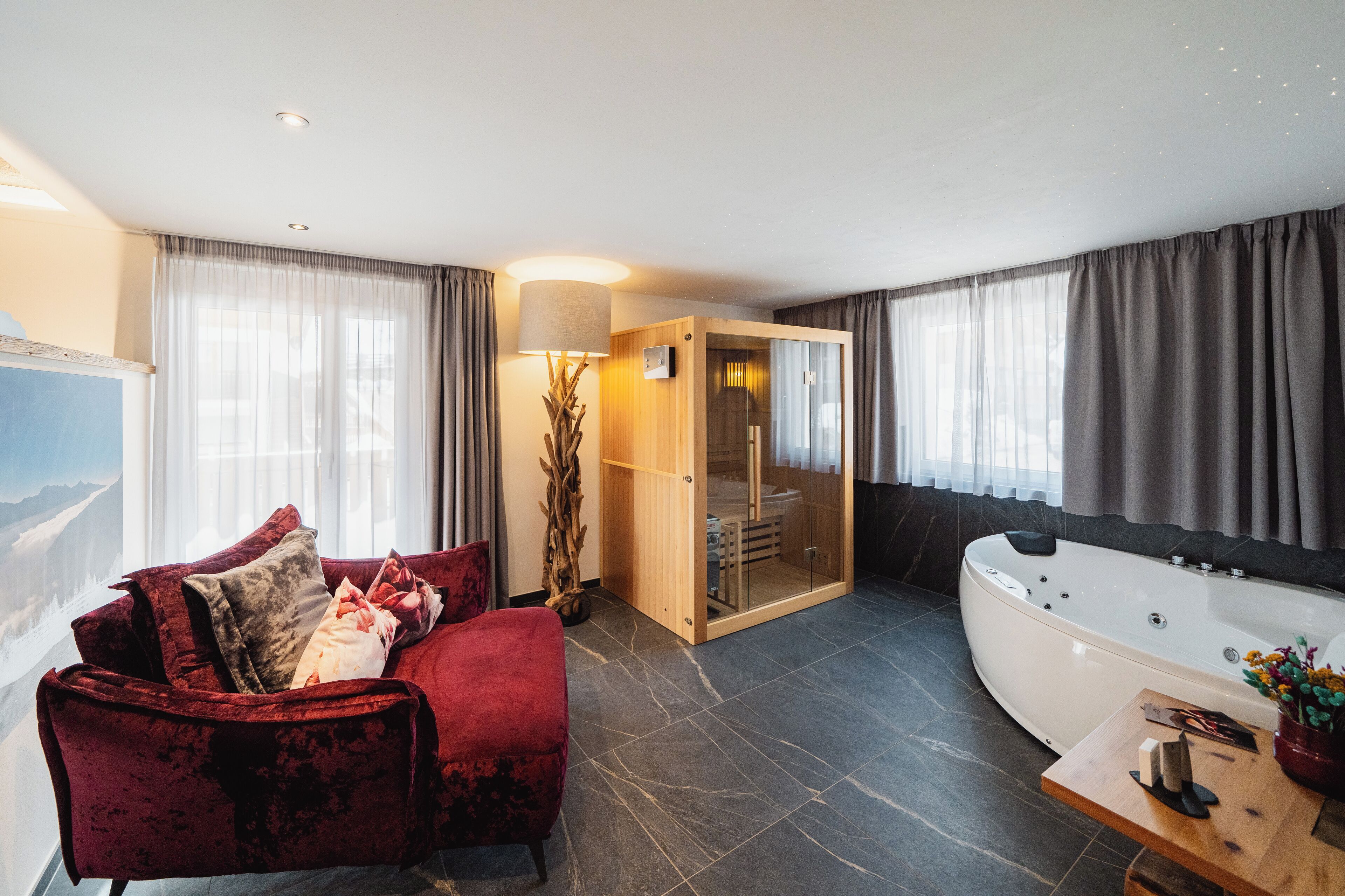 A modern bathroom with a large bathtub, a red velvet chair, and a wooden table with toiletries.