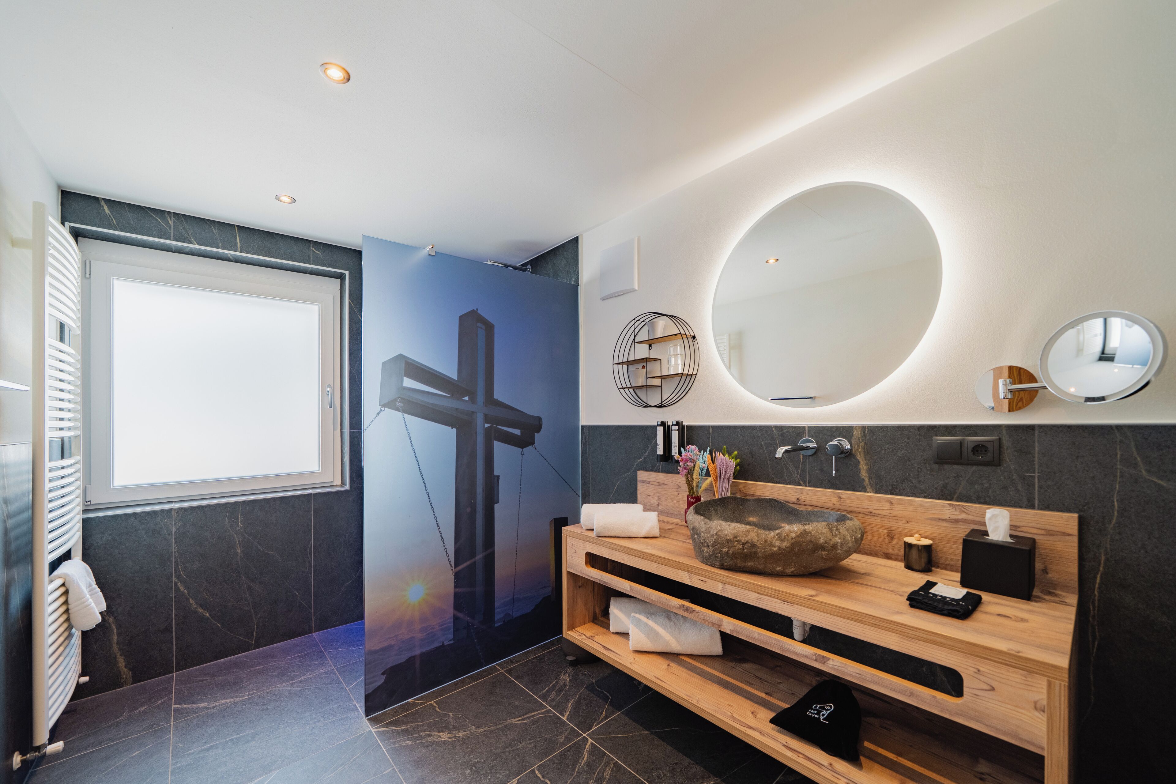 Un bagno moderno con un mobile bagno in legno, uno specchio grande e una croce appesa al muro.