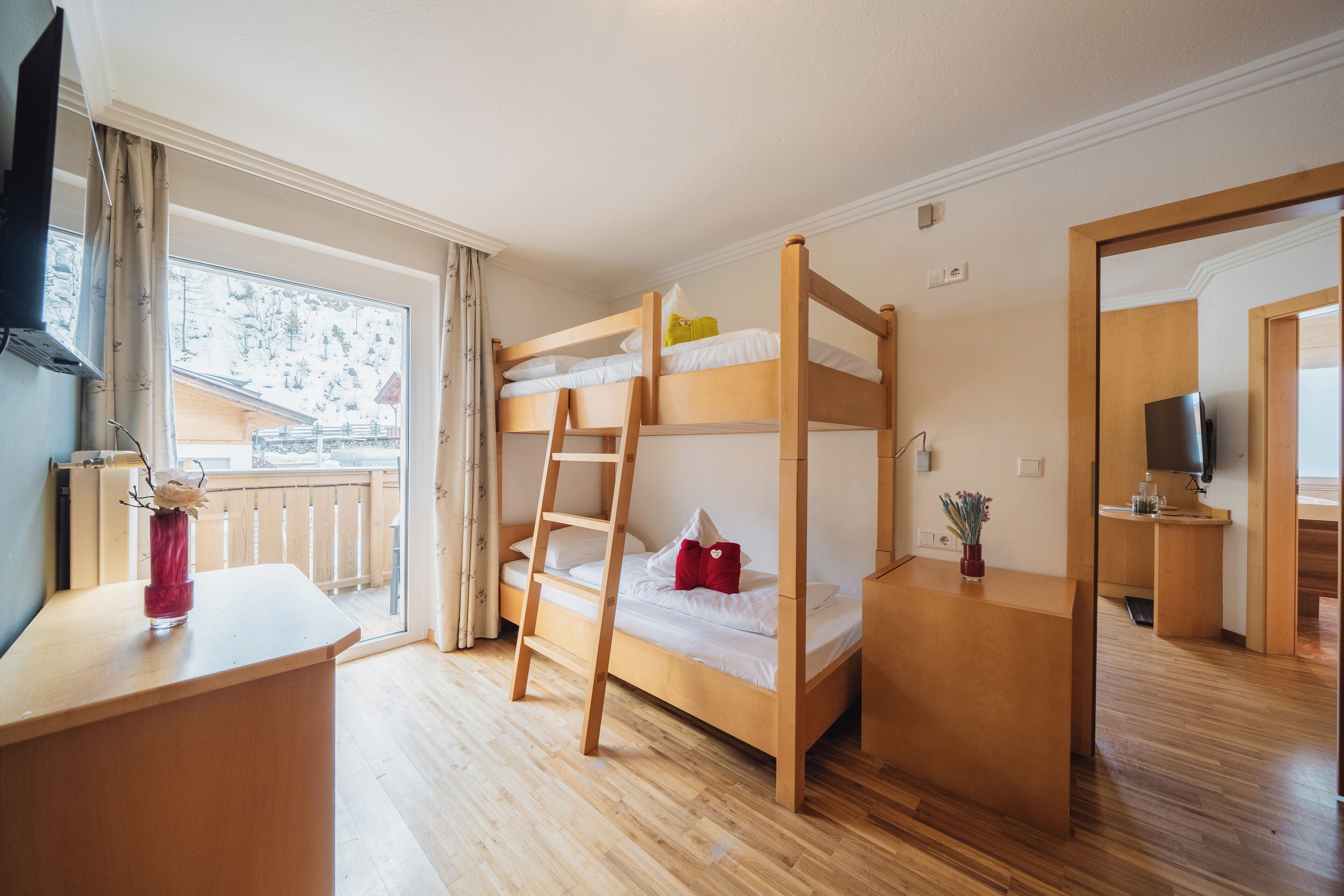 Habitación con literas, un escritorio de madera, una escalera y una pequeña mesa con un florero.
