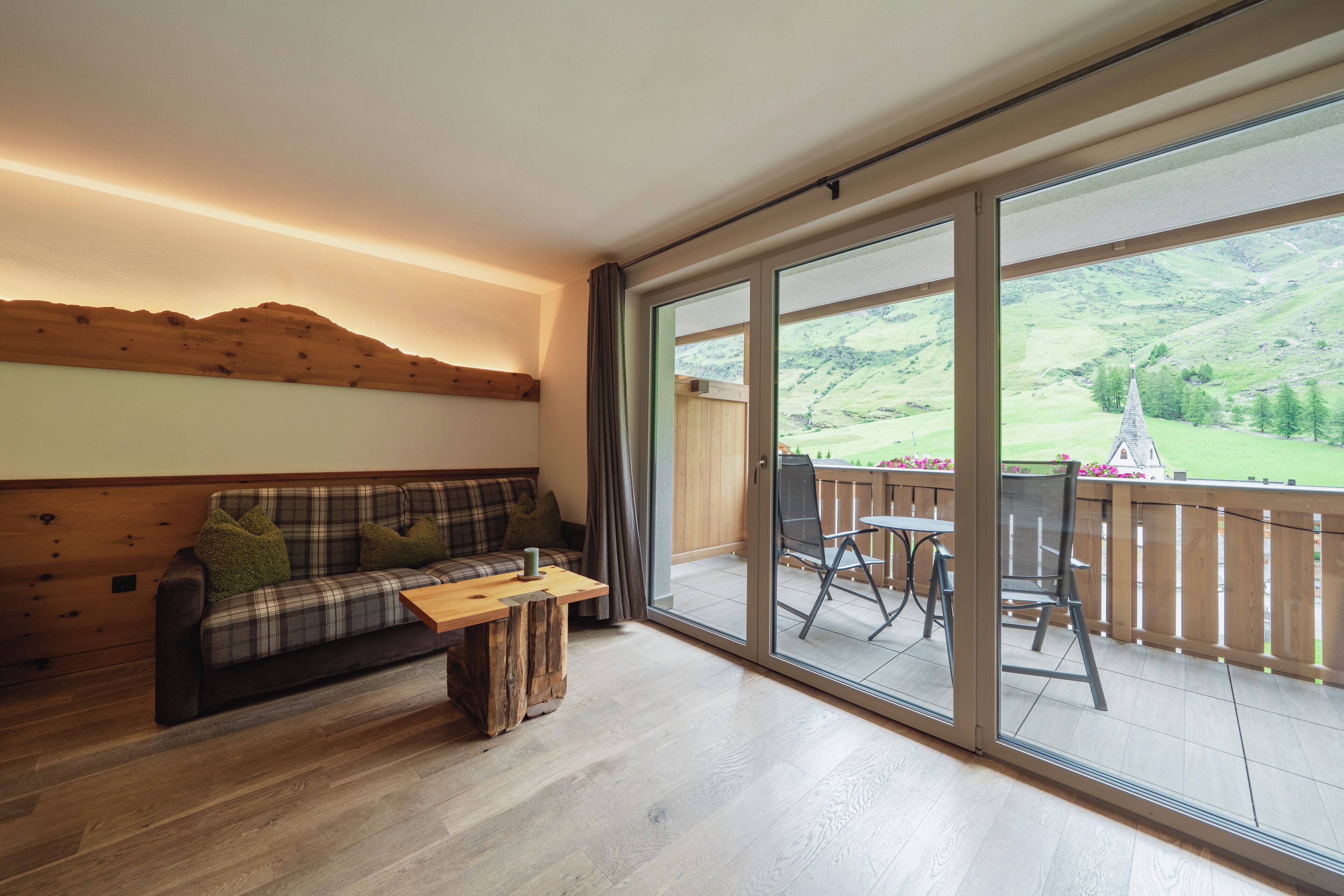 A cozy living room with a wooden sofa, a coffee table, and a balcony with a table and chairs.