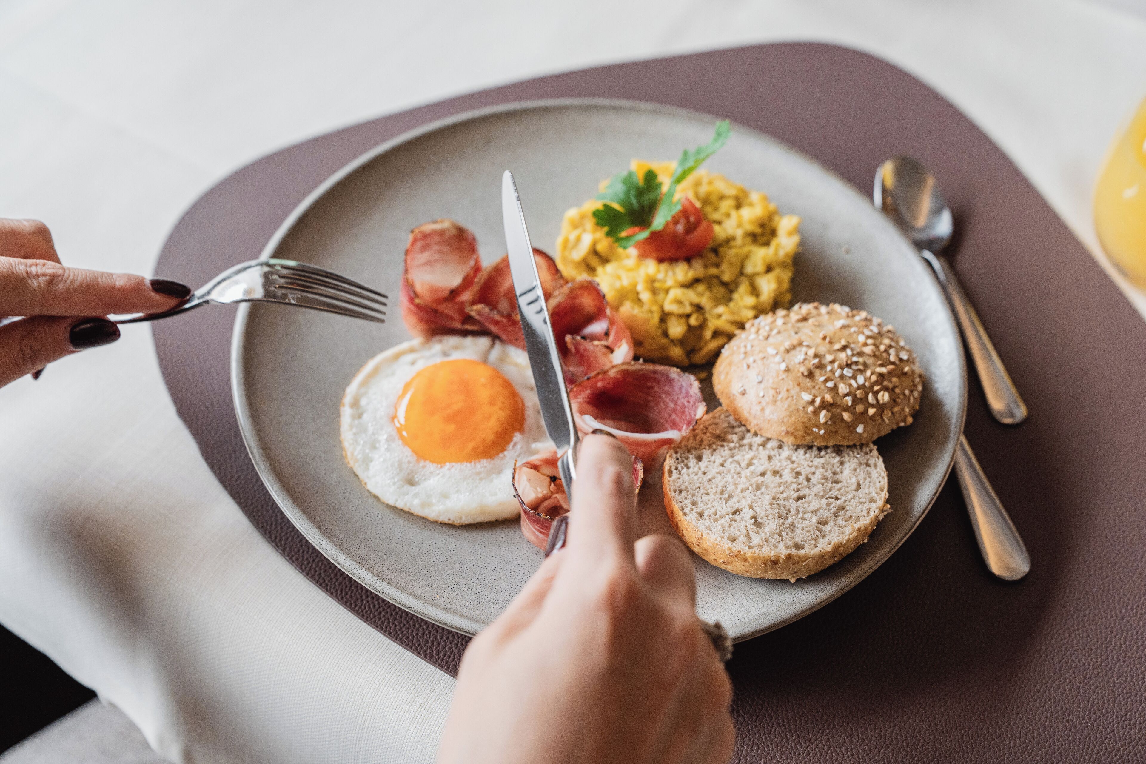 Une assiette de petit-déjeuner comprenant des œufs, du bacon, des œufs brouillés et un pain aux graines de sésame.