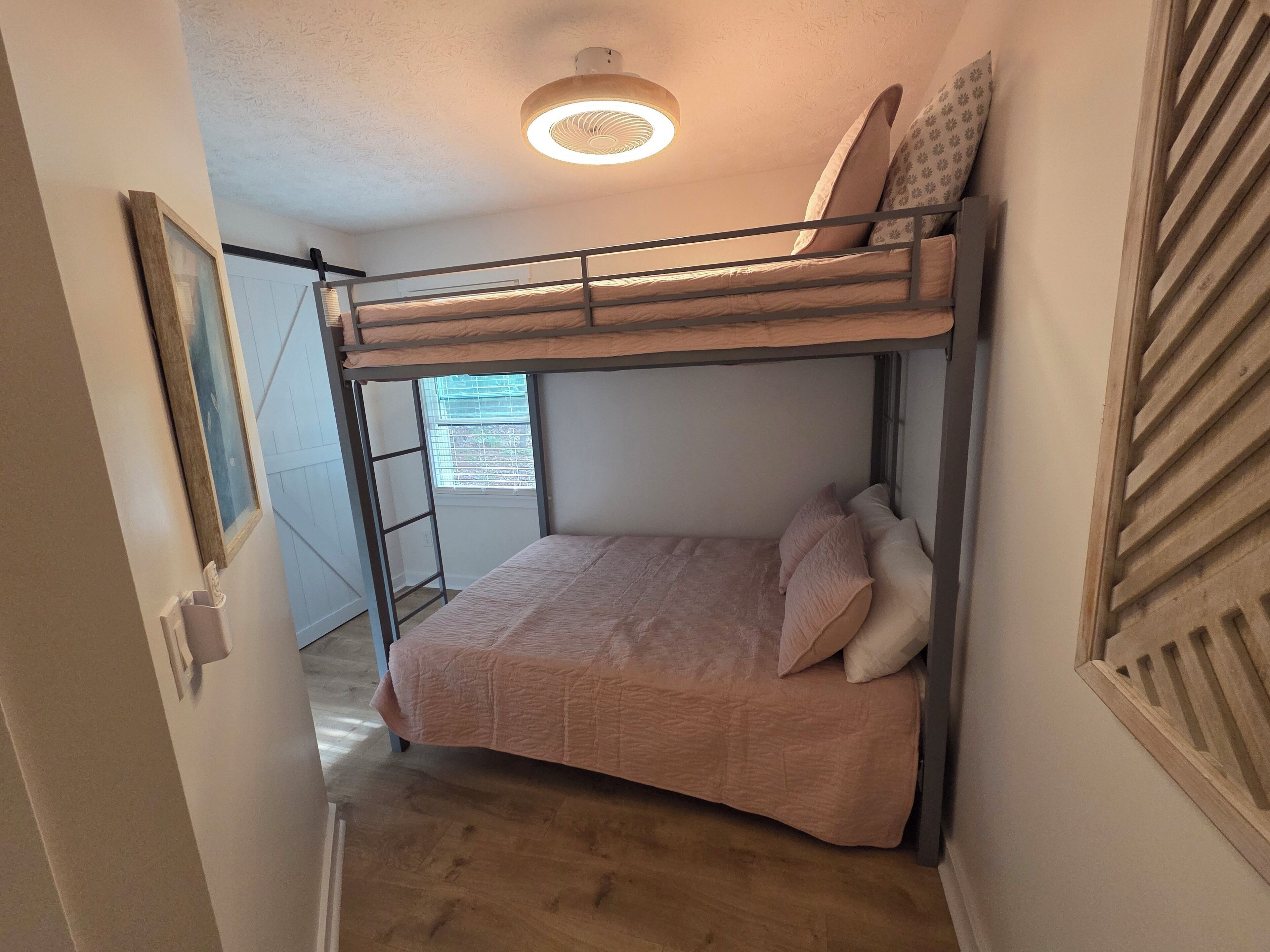 A bunk bed room with a ladder, a window with blinds, and a ceiling light.