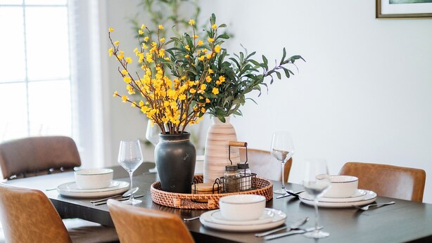 A dining table set with white plates, bowls, and glasses, accompanied by a vase of yellow flowers and a candle holder.