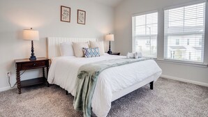 A bedroom with a bed, two bedside tables, two lamps, and a window with blinds.