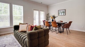 A living room with a sectional sofa, dining table, chairs, and a large window with blinds.
