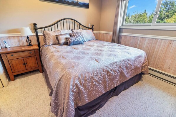 A bedroom with a bed, a nightstand, a lamp, and a window with a view of trees.