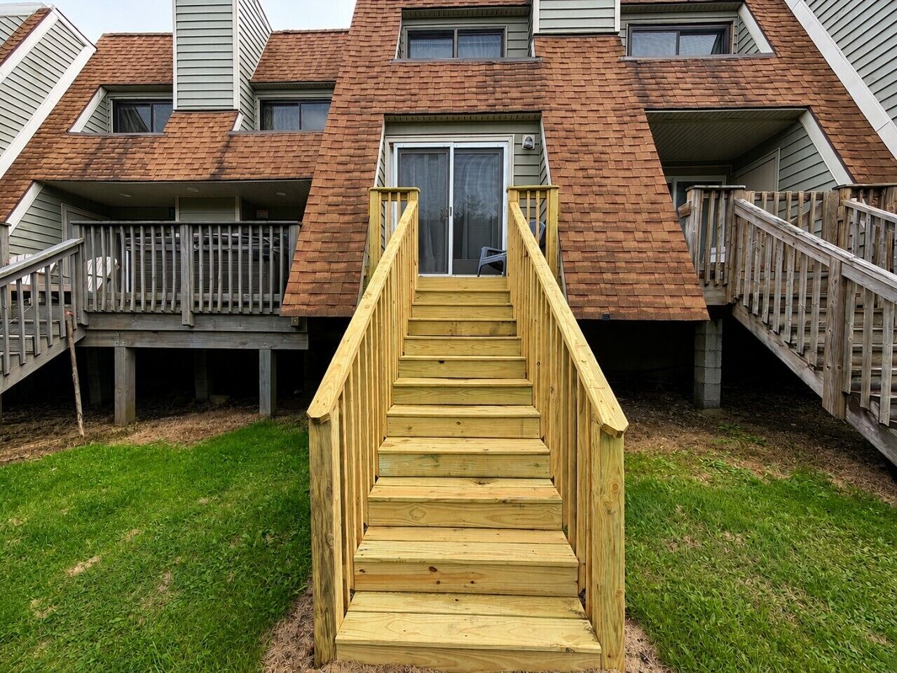 Un escalier en bois mène à un immeuble d’habitation dont la façade est en briques et qui possède de nombreuses fenêtres.
