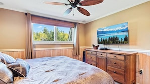 A bedroom with a large bed, wooden dresser, and a television on the wall.