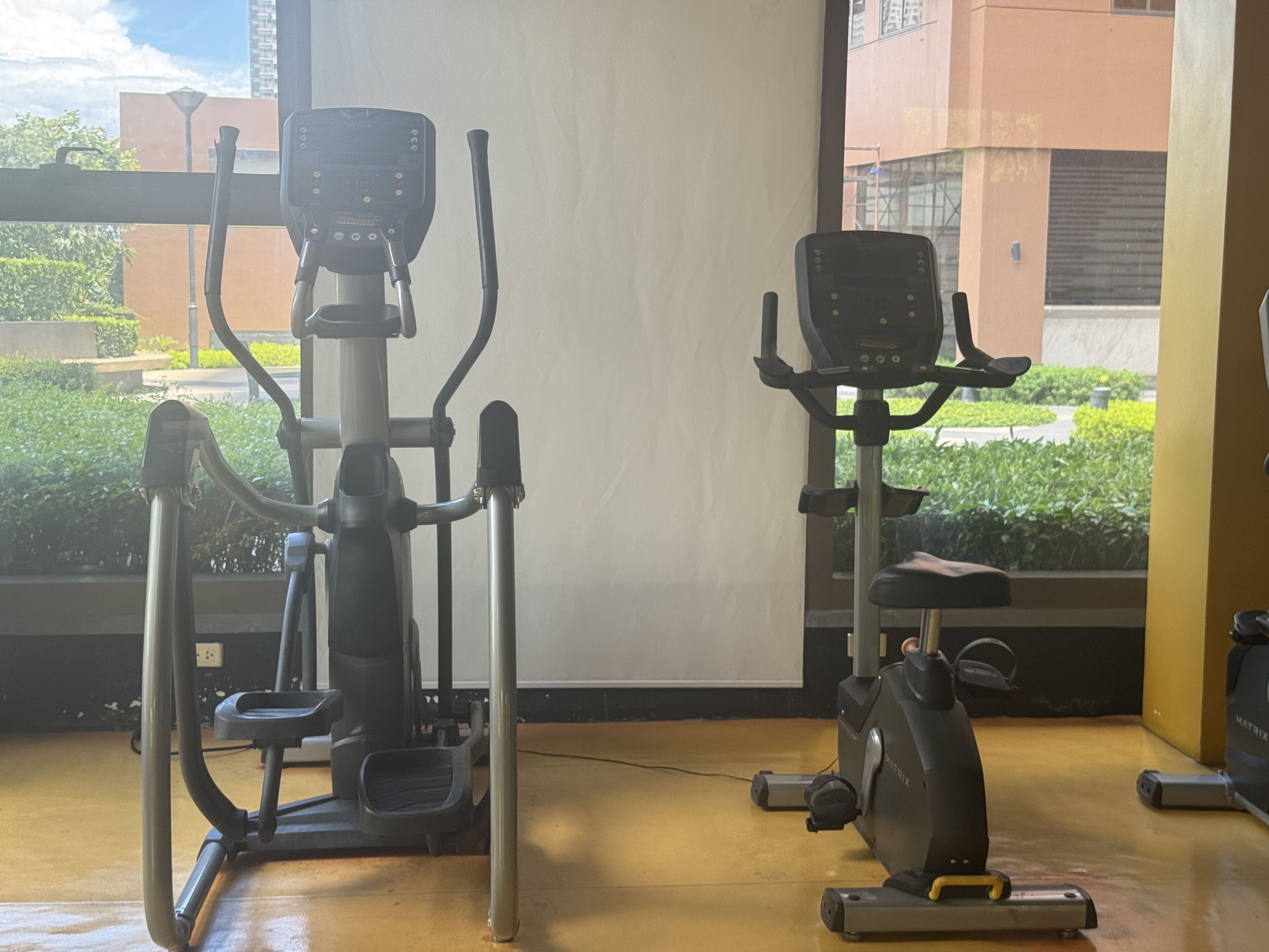 Two stationary bikes in a room with a view of greenery and buildings outside.