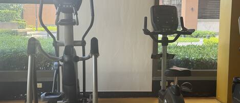 Two stationary bikes in a room with a view of greenery and buildings outside.