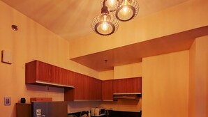 Une cuisine compacte avec des meubles en bois, un réfrigérateur encastré, une table à manger avec des chaises et des luminaires suspendus.
