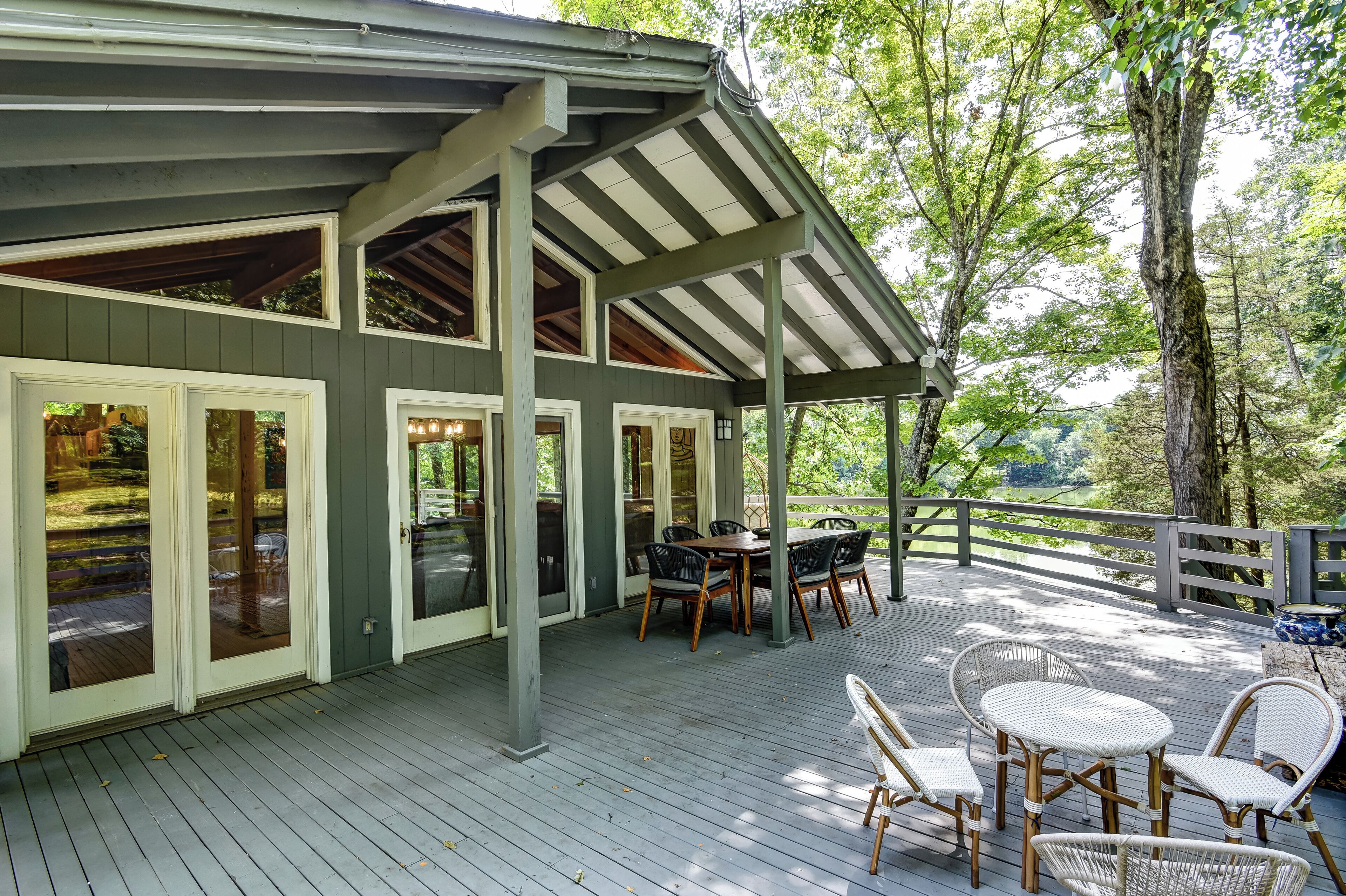 A covered outdoor deck with a dining area, wooden chairs, and a table.
