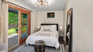 Un dormitorio con cama, lámparas de noche, un espejo grande, una ventana con cortinas y vistas a zonas verdes.