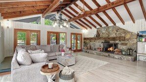 Amplia sala de estar con chimenea de piedra, vigas de madera y ventanas grandes.