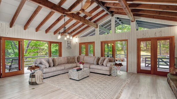 Amplia sala de estar con un sofá modular grande, vigas de madera, ventanas amplias y vistas al exterior.