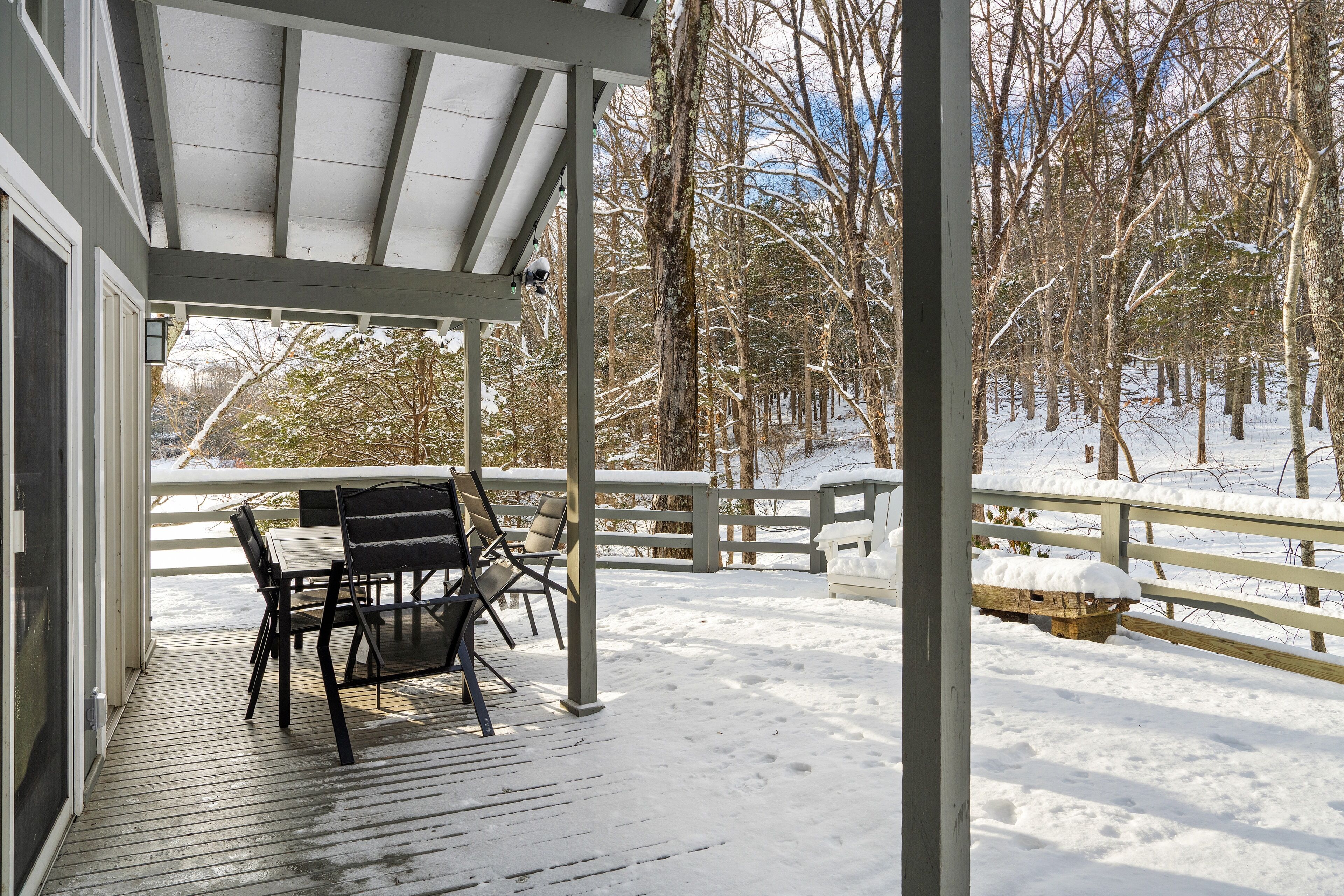 A covered outdoor seating area with a table and chairs, surrounded by a wooden deck and a snow-covered landscape.