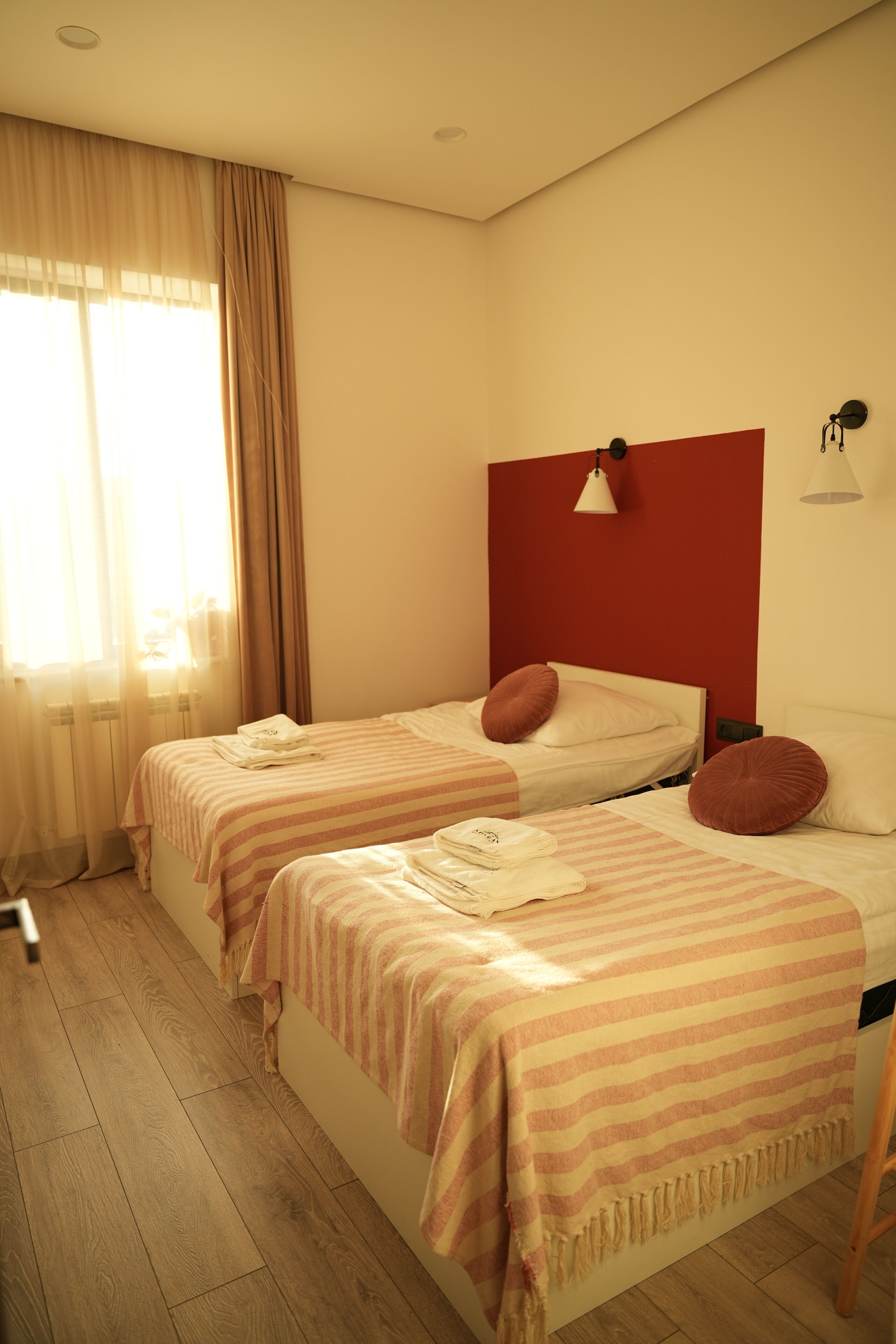 Ein Hotelzimmer mit zwei Betten, einer roten Akzentwand und einem großen Fenster mit Vorhängen.