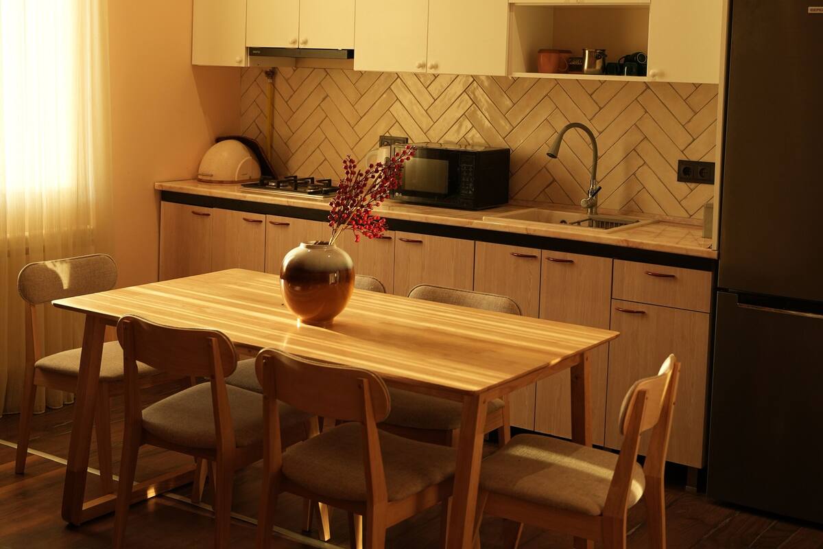 A modern kitchen with white cabinets, a wooden dining table, and a refrigerator.