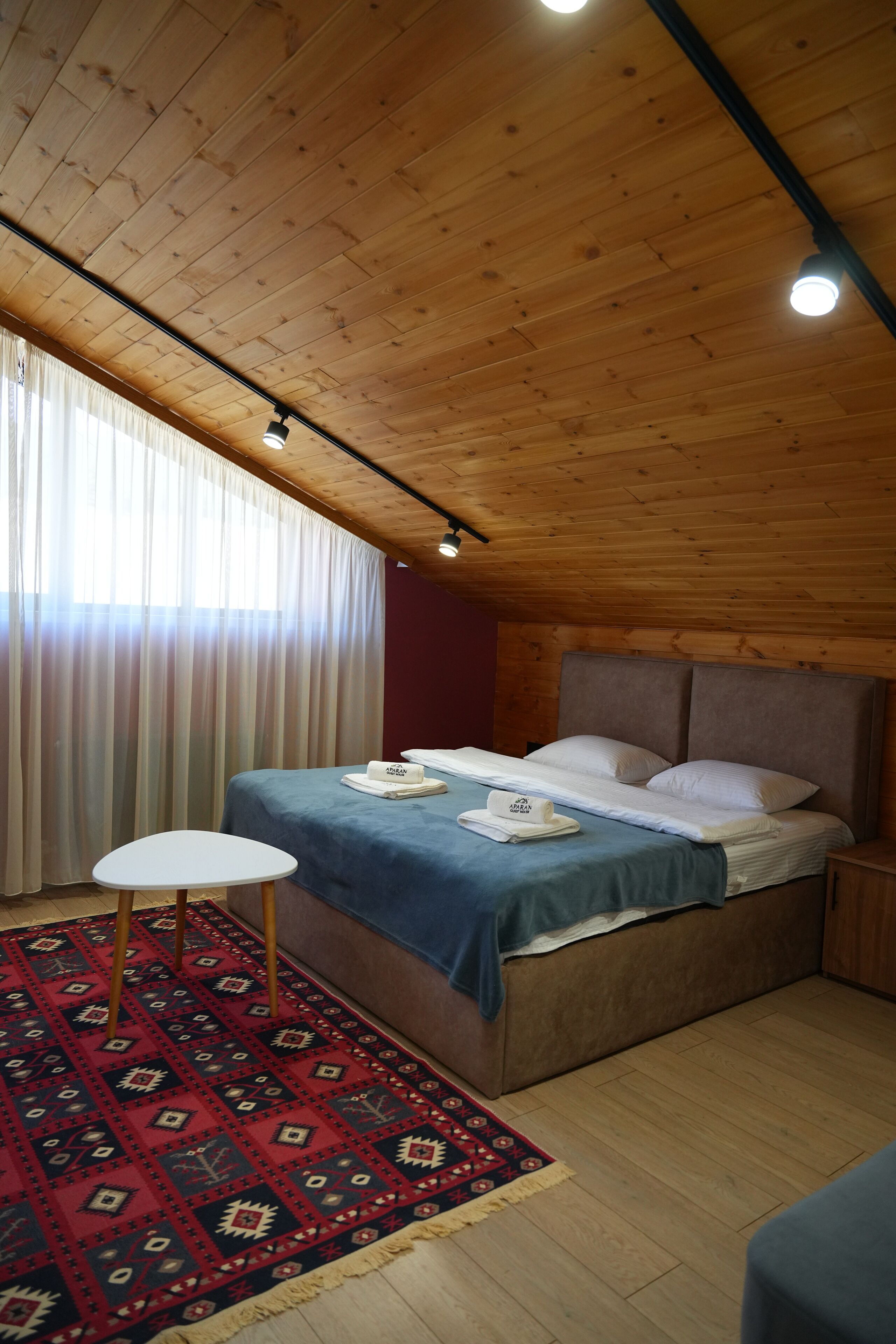 Una habitación con paneles de madera, una cama, una mesita y un tapete estampado.