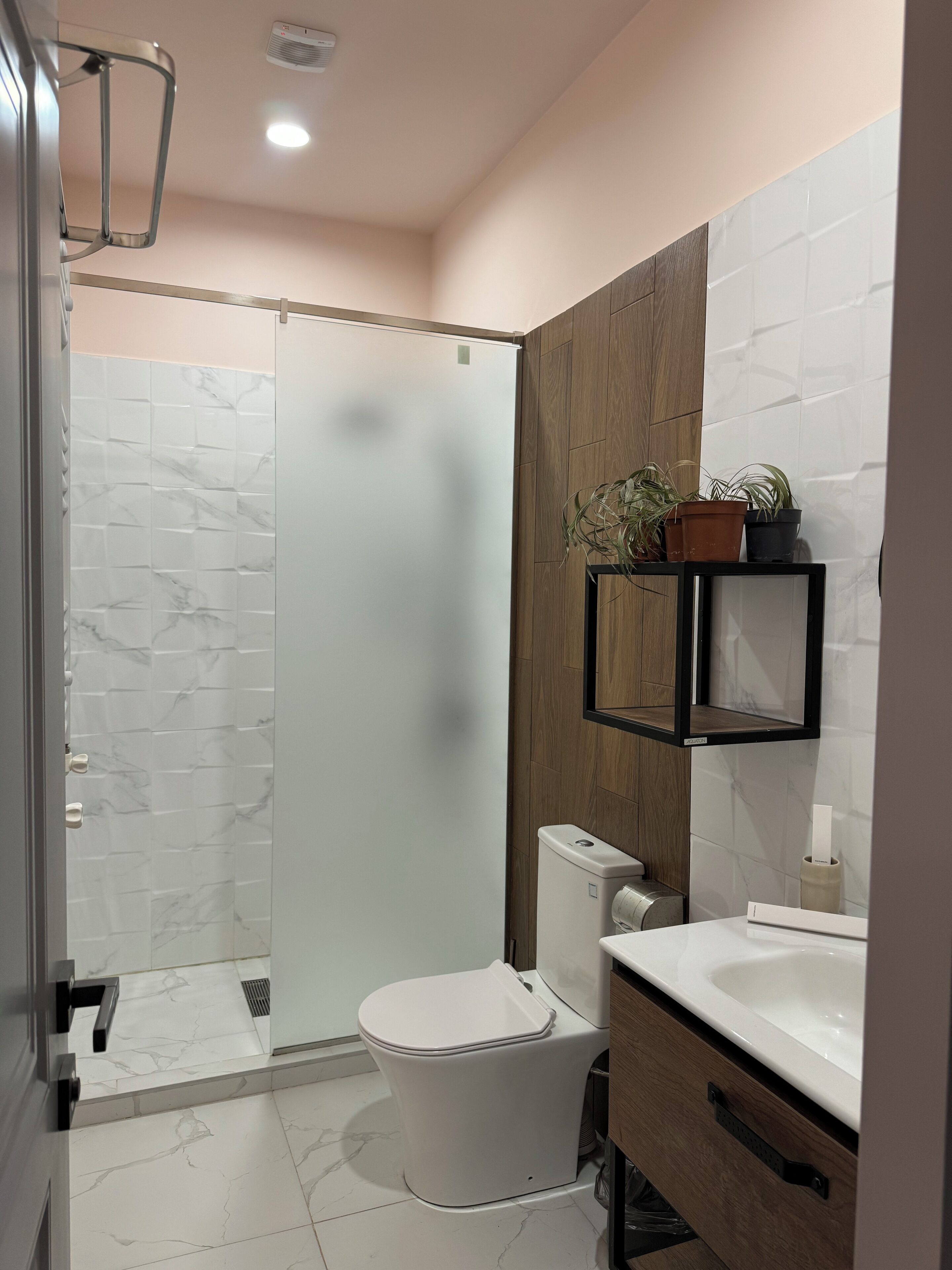 Een moderne badkamer met een douchecabine van glas, een toilet, een wastafel en een houten wastafelmeubel.