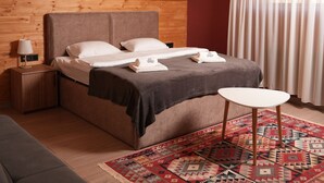 Un dormitorio con techo de madera, cama con ropa de cama blanca, mesita de noche con lámpara y alfombra estampada.