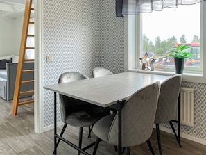 A dining area with a table and chairs, a window with a view of the outside, and a ladder leaning against the wall.
