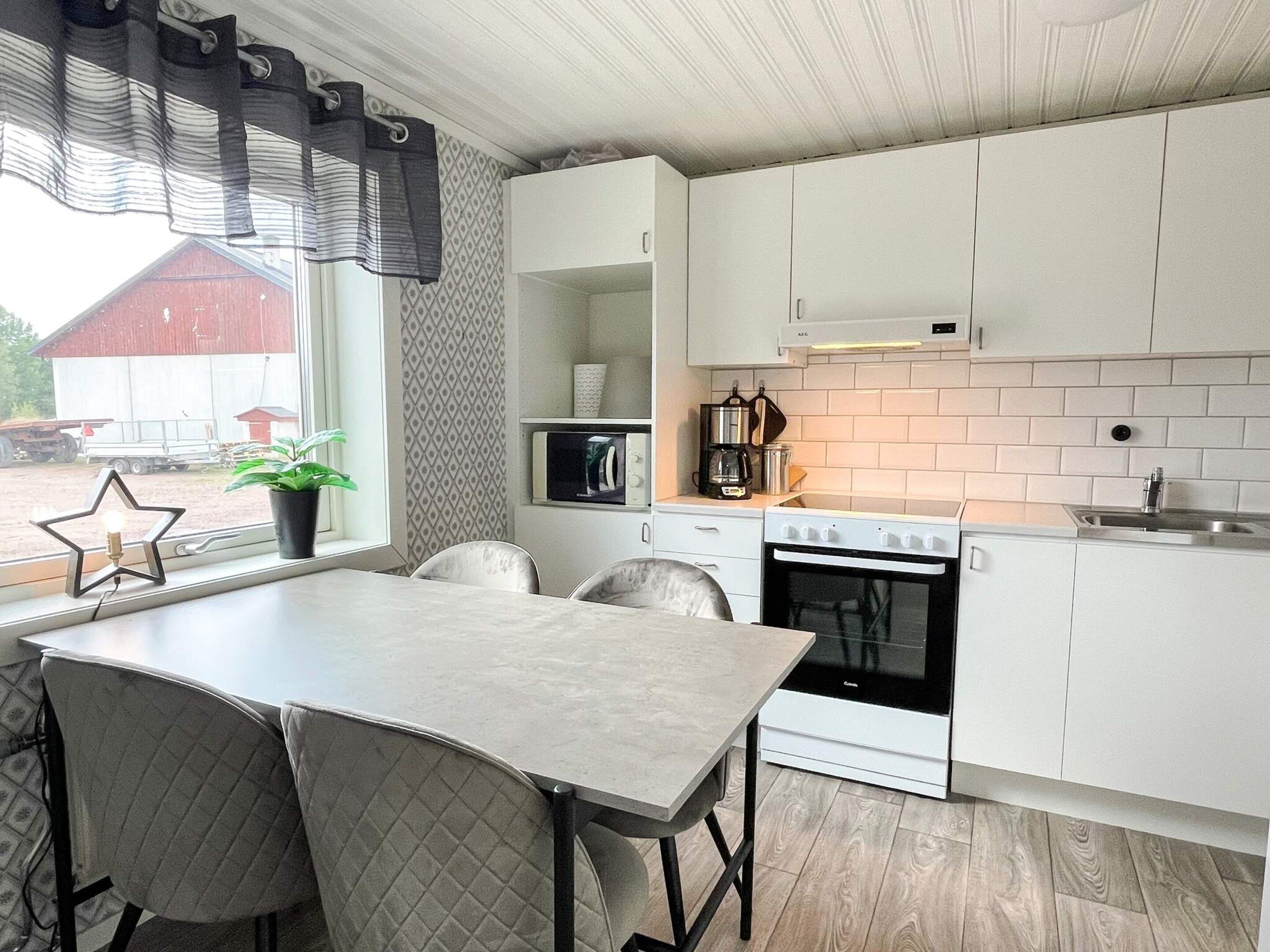 A modern kitchen with white cabinets, a stove, a microwave, and a dining area with a table and chairs.