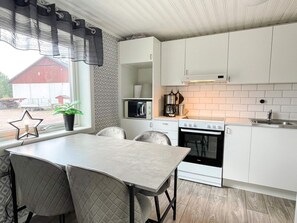 A modern kitchen with white cabinets, a stove, a microwave, and a dining area with a table and chairs. - 4 Person Holiday Home in Berga (Berga)