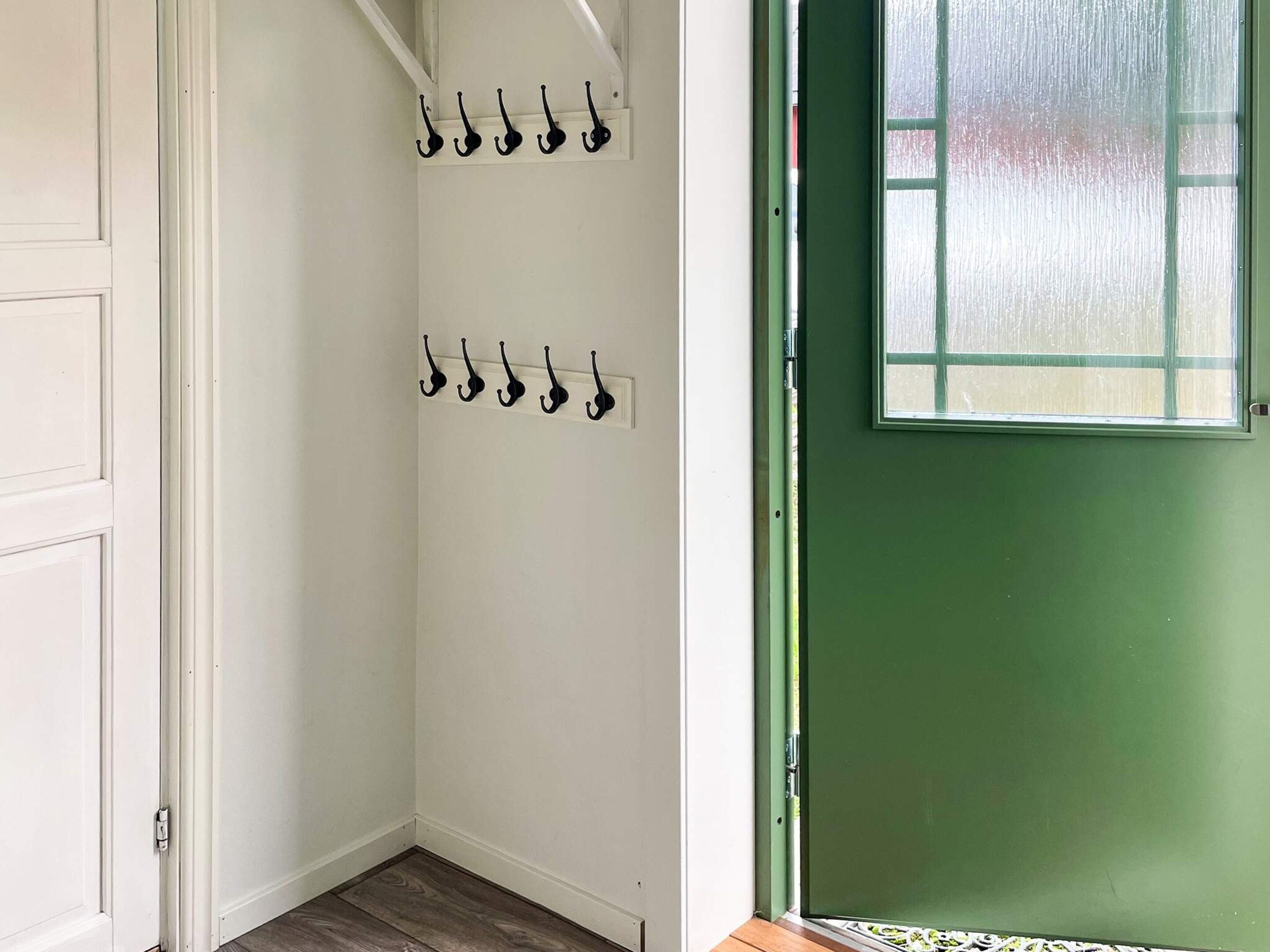 A room with a green door, white walls, and a wooden floor. There are two sets of black hooks on the wall.