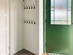 A room with a green door, white walls, and a wooden floor. There are two sets of black hooks on the wall.