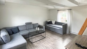 A modern living room with a grey sectional sofa, a small sofa with cushions, a coffee table, and a window with curtains. - 4 Person Holiday Home in Berga (Berga)
