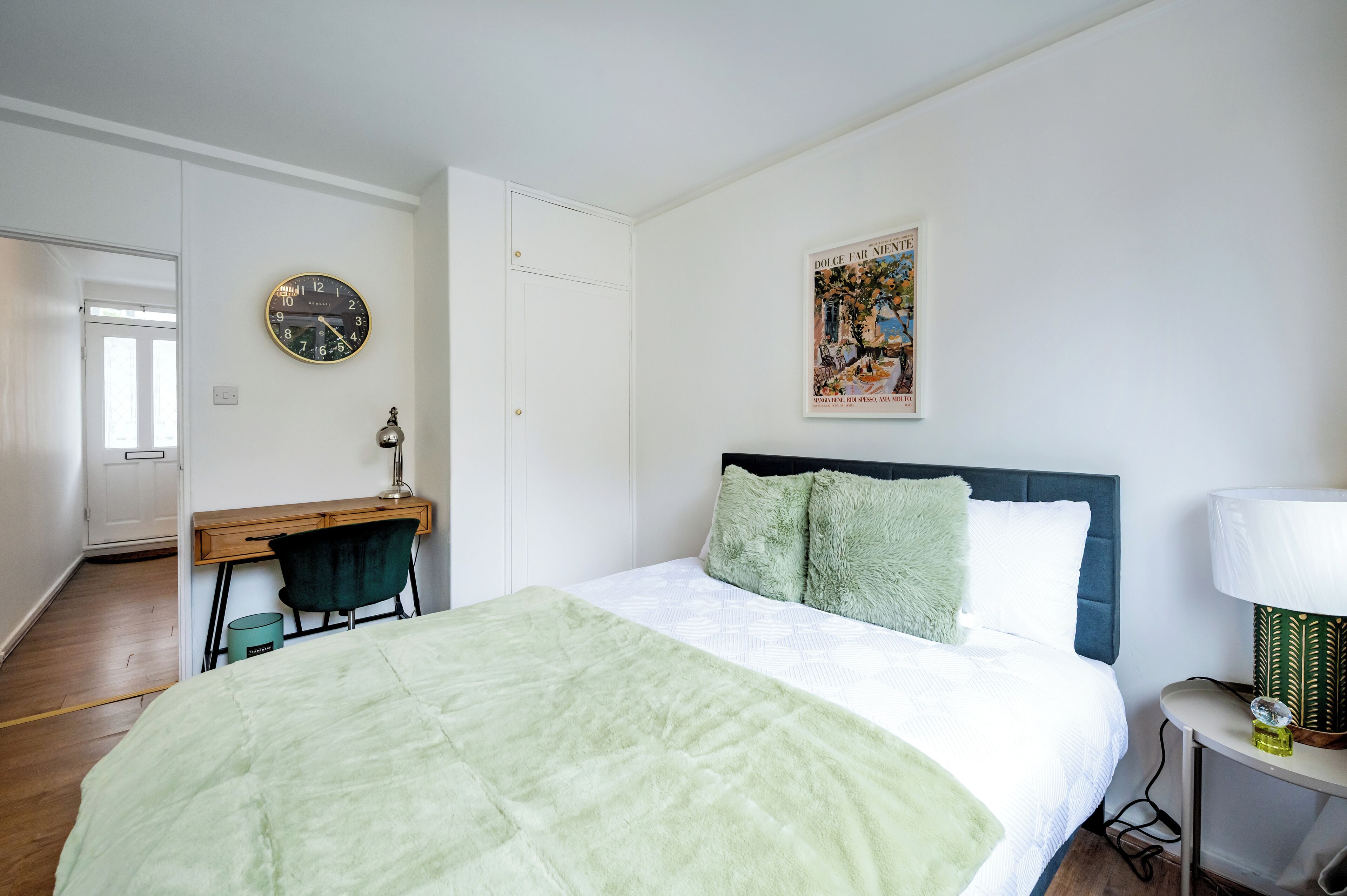 Une chambre à coucher avec un lit, un bureau, une chaise, une horloge et un tableau encadré au mur.