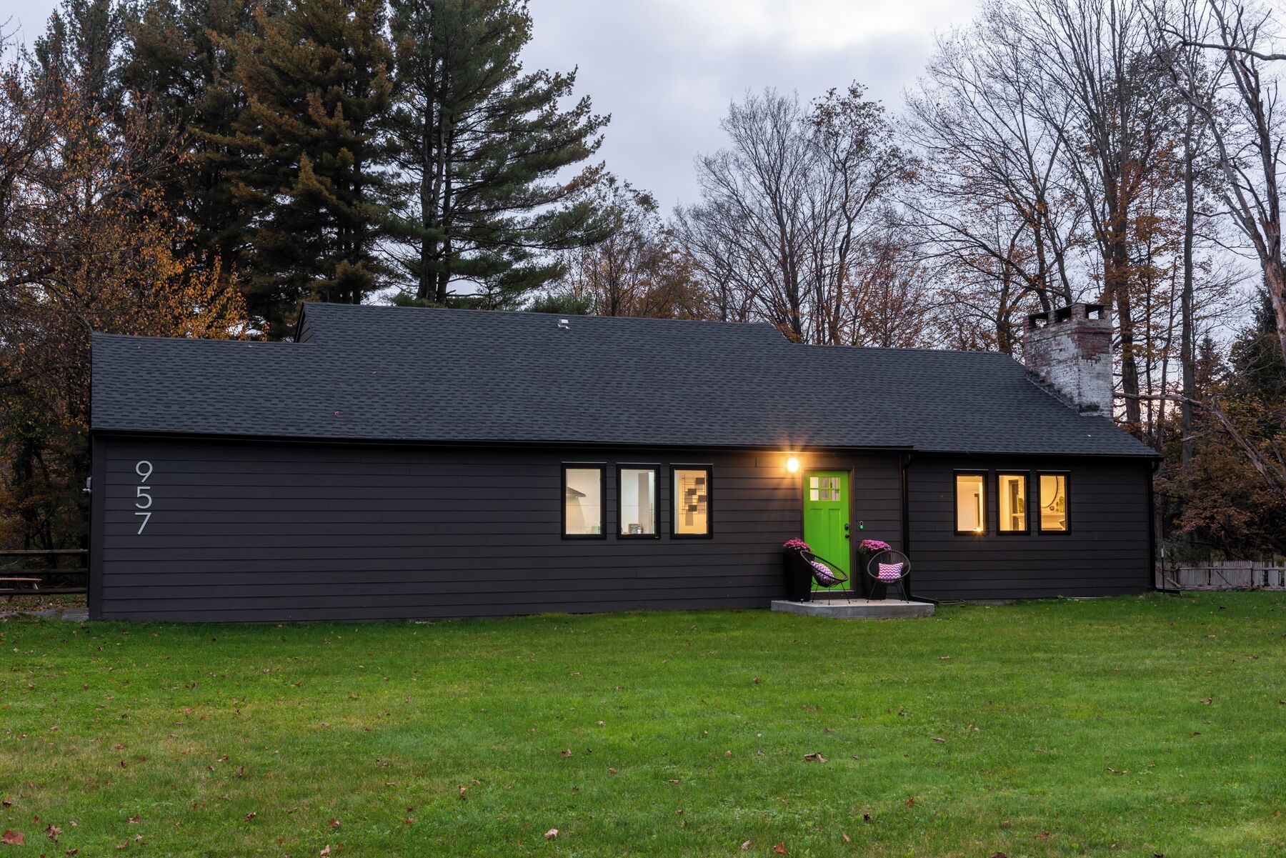 A black house with a green door, numbered 957, and a small porch with a chair.