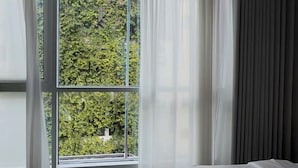 A bedroom with a large window, a bed, and a view of greenery outside. - J Village Hotel - Triệu Việt Vương (Hanoi)