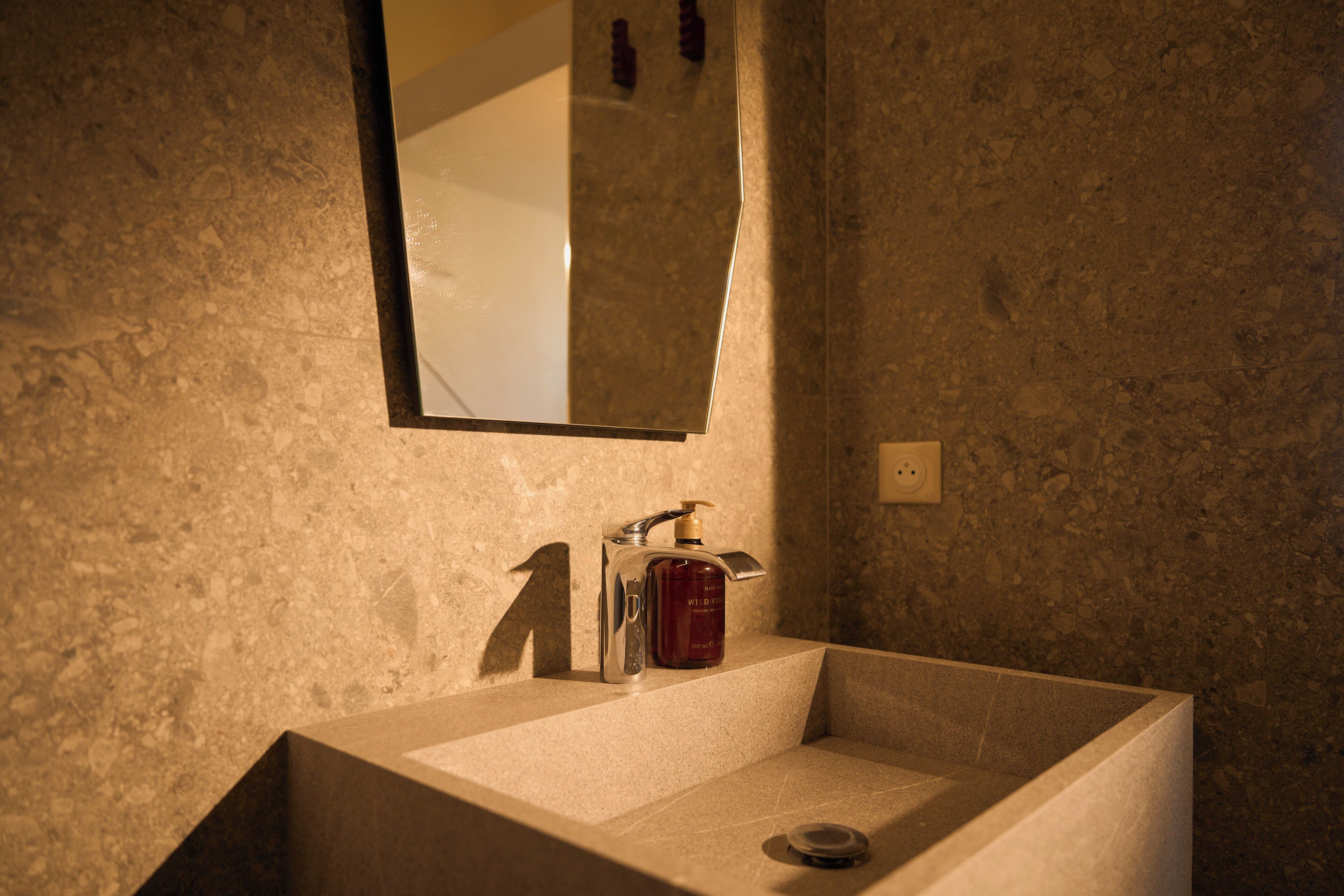 A bathroom with a rectangular sink, a mirror, and a bottle of Wild brand soap.