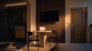 A modern hotel room with a bed, a small round table with two chairs, a television mounted on a wooden wall, and a wooden door. - Atypical suite with private jacuzzi - downtown Cognac (Cognac)