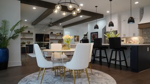 Une cuisine moderne dotée d’un îlot central, de luminaires suspendus et d’un coin repas avec des chaises blanches et une table ronde.