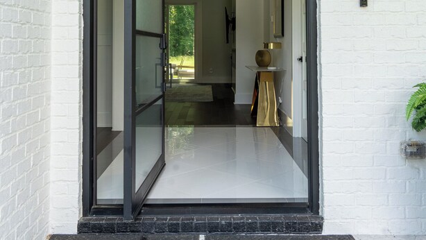 Une entrée moderne avec une porte en verre, un mur en briques blanches et une petite table sur laquelle est posé un vase.