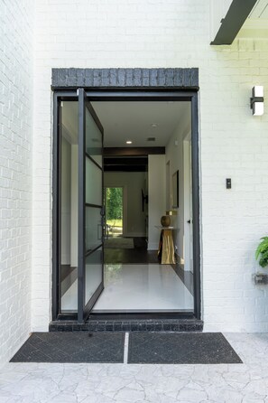 A modern entrance with a glass door, a white brick wall, and a small table with a vase.