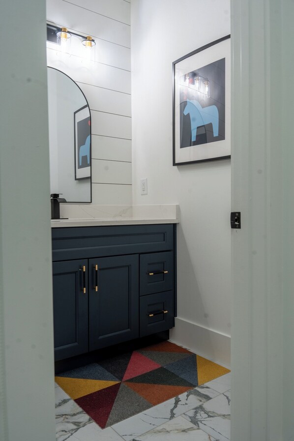 A bathroom with a white vanity, dark cabinets, a colorful rug, and a framed picture on the wall.