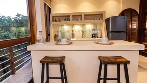 A modern kitchen with a central island, two stools, a refrigerator, and a view of greenery outside. - Ocean Views w/ Rooftop Lounge (Mazunte)