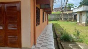 A house with a wooden double door, a tiled pathway, and a small garden with plants and a tree. - Studio for 2 persons (Ebolowa, Région du Sud)