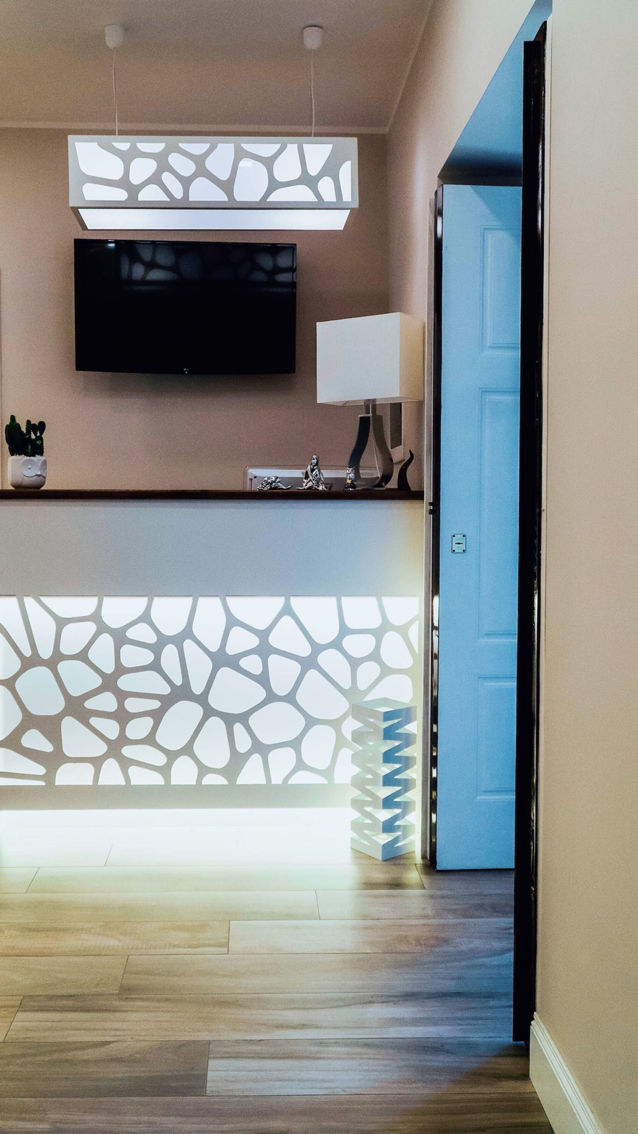 A reception area with a flat-screen TV mounted on the wall, a decorative light fixture, and a patterned wall feature.