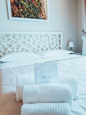 Una cama bien hecha con sábanas y almohadas blancas, un cabecero decorativo, un cartel que dice 