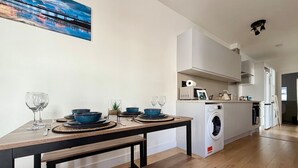 A modern kitchen with a built-in washing machine, a dining table set with blue bowls and wine glasses, and a bench.
