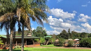 A grassy area with a gazebo, a covered seating area, and a building with a green roof. - El manantial de Iguazu (Puerto Iguazú)