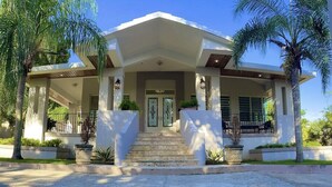 Une maison moderne dotée d’un porche avant couvert, de palmiers et d’une pelouse bien entretenue.