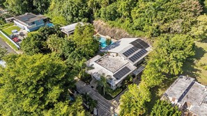 Vista aérea de una propiedad residencial con paneles solares, piscina y vegetación densa alrededor.
