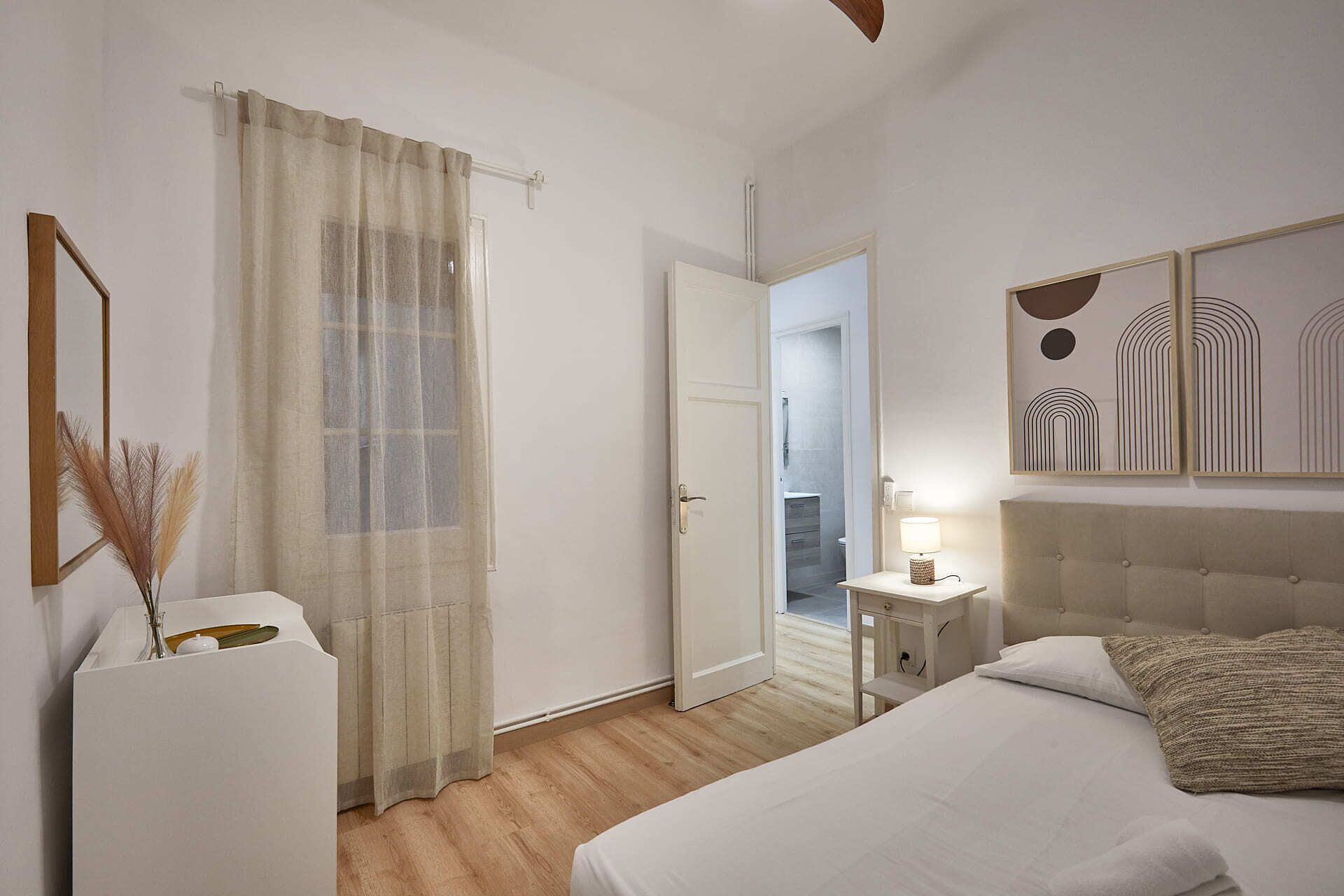 A bedroom with a bed, a bedside table, a lamp, a mirror, and a door leading to a bathroom.