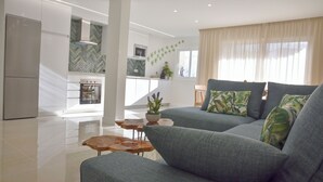 Uma sala de estar moderna com um sofá, uma mesa de centro e uma cozinha ao fundo.